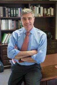 Attorney sitting on desk in front of book shelf with jacket on